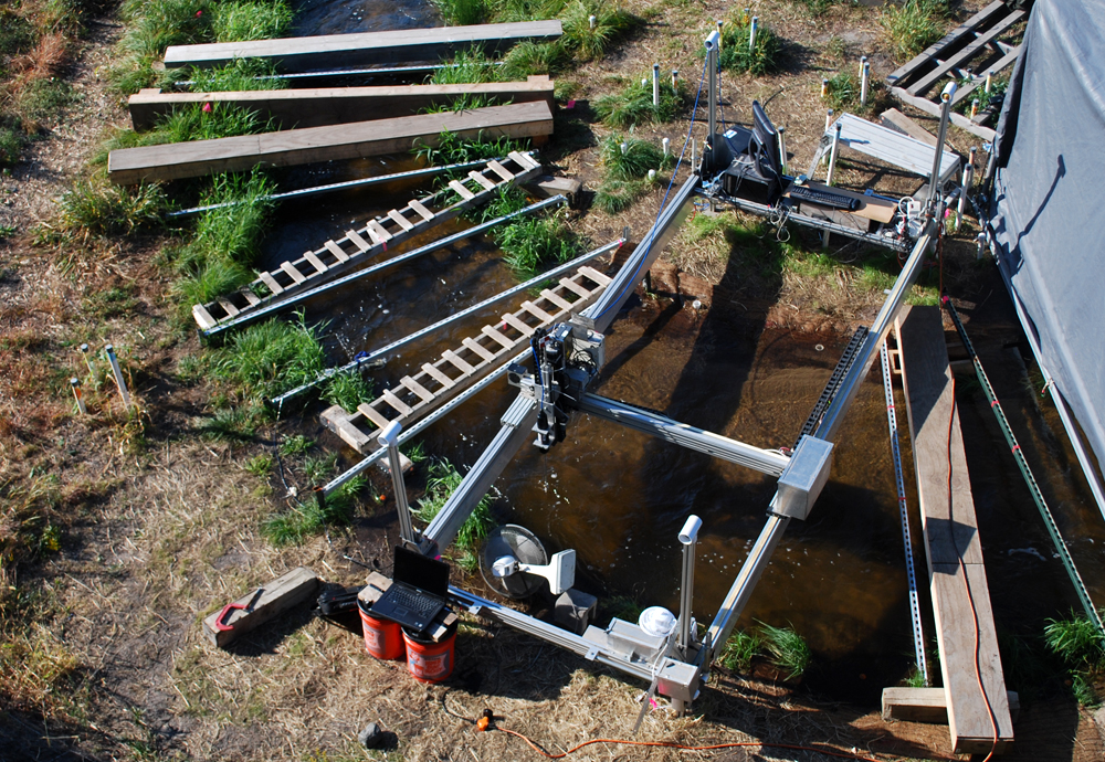 An overview of the experimental setup at the Outdoor StreamLab, including the mechanized cart supporting the acoustic Doppler velocimeter and spectrometer (Credit: Carl Legleiter)