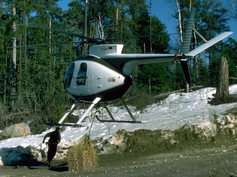 A Hughes 500 chopper picking up a sling of concentrated sulphuric acid for a study on the effects of acid rain on lake ecosystems. (Credit: John Shearer)