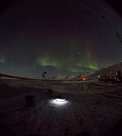 The northern lights shimmer above as Jonathan Cohen measures atmospheric light during the Arctic’s polar night. (Credit: University of Delaware)