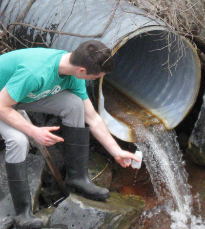 Shane DeGaetano, a senior in Biological and Environmental Engineering at Cornell University, collects storm water near Cascadilla Creek in Ithaca, New York. The water was analyzed for chloride associated with road salt. (Credit: Lauren McPhillips)