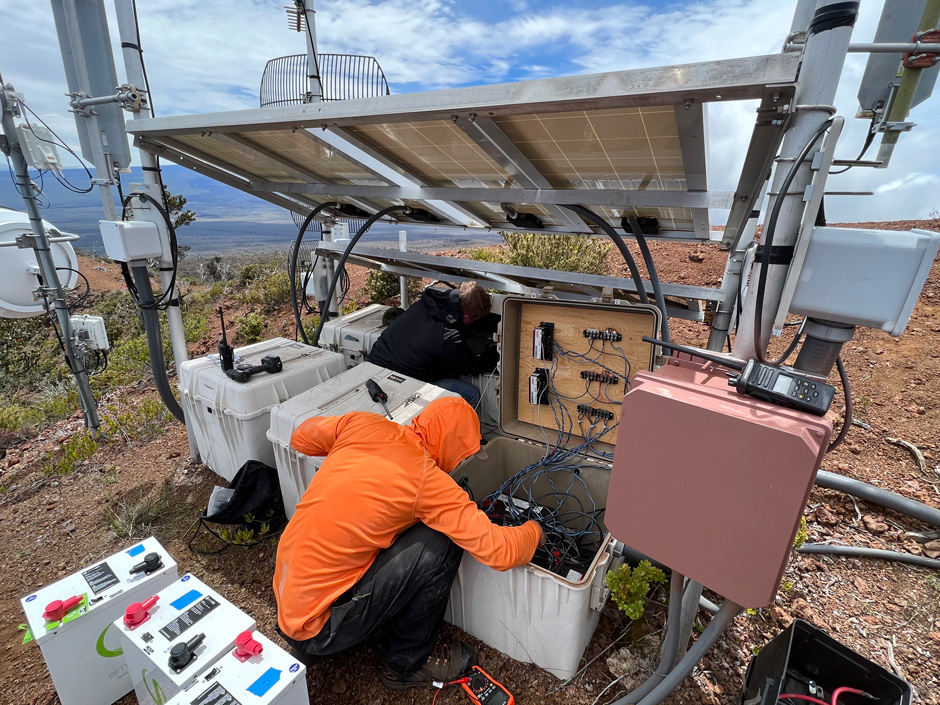 A Hawaiian Volcano Observatory technician replaces batteries on the Hualālai repeater station. The station, which relays monitoring signals from nearby stations back the observatory, is powered by batteries that store energy generated by solar panels. 