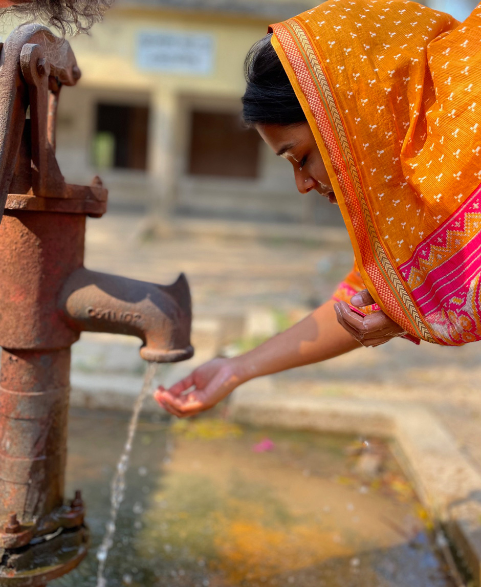 A Chemists Without Borders volunteer, wearing a bright orange scarf, takes a break from her work and washes at one of the many hand-pumped wells in the area.