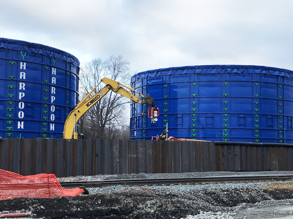 Sheet piling is installed around the two blue lake tanks as a method for secondary containment. The lake tanks will temporarily stage wastewater from the derailment site while trucks transport these liquids off-site for disposal.