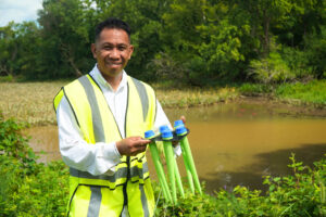 Co-founder and CEO of ecoSPEARS Sergie Albino standing in front of a small pond holding his remediation tool, ecoSPEARS.