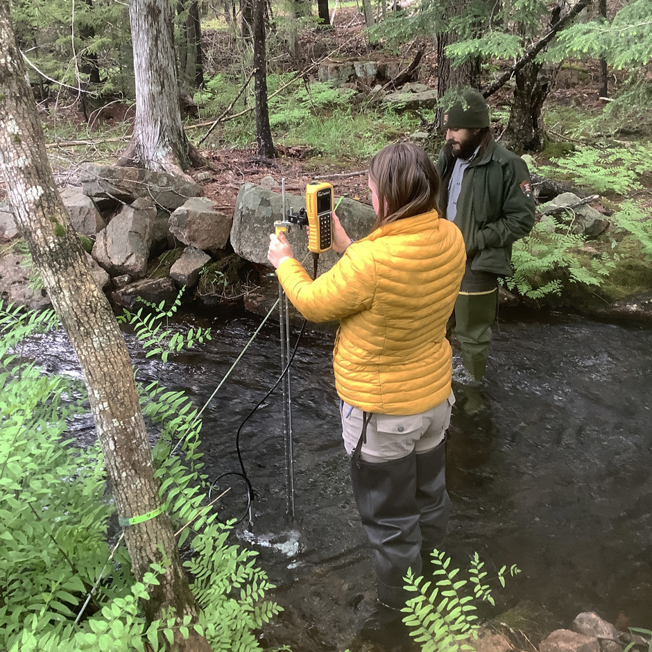 Acadia NP Biologist Kathleen Brown and Biological Technician Jake Van Gorder measure streamflow during a monthly stream monitoring visit.