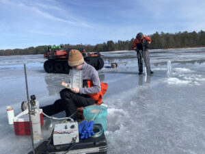 Trout Lake Research Station scientists sit on an ice covered lake and conduct water and ice measurement.
